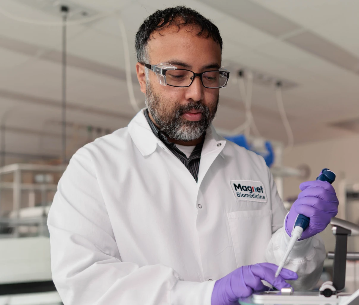 Scientist wearing a white lab coat and purple gloves, using a pipette